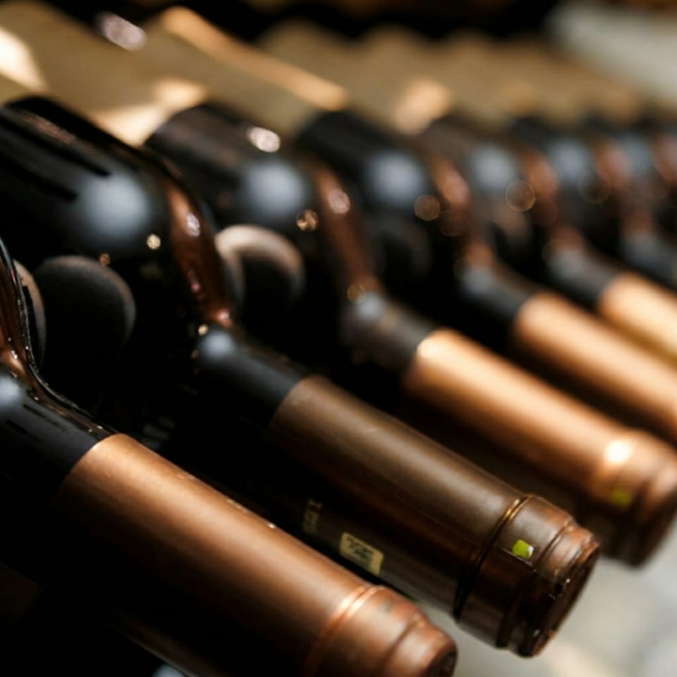 Row of dark wine bottles with gold foil tops stored in a wine rack.